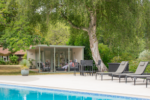 Contemporary garden room with a covered veranda and outdoor seating, positioned beside a swimming pool.